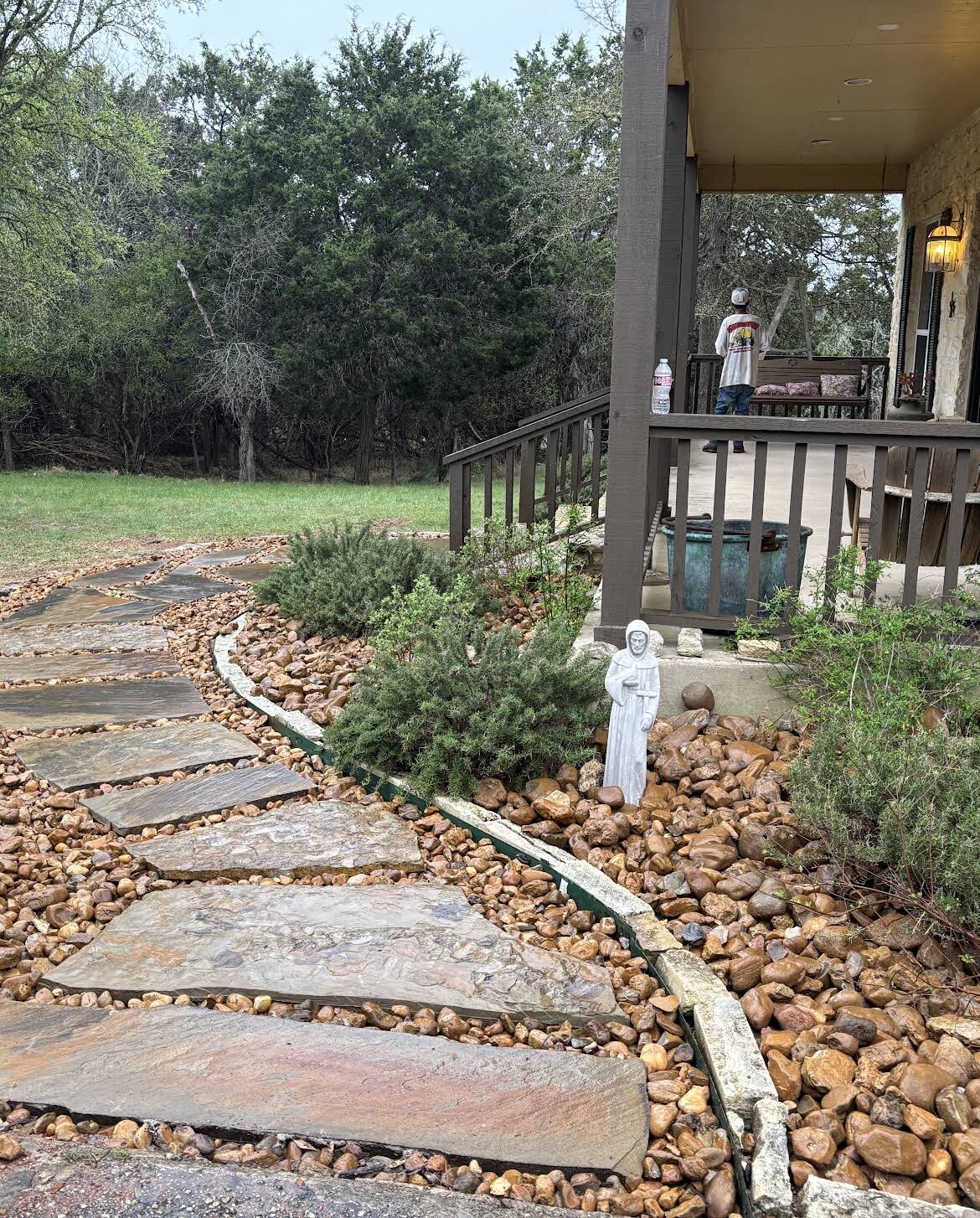 flagstone walkway through river rock with shrubs toward porch